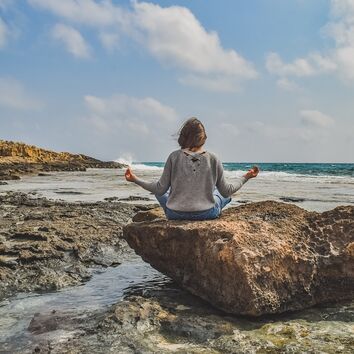 Frau im Yogasitz auf einem Felsen im Meer